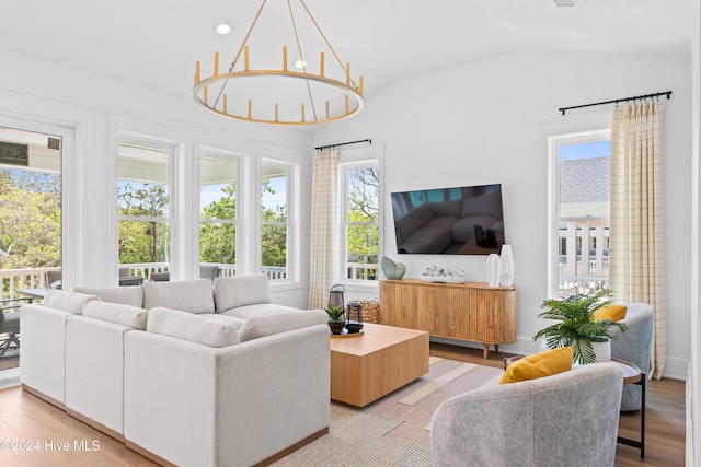 living room with an inviting chandelier, a healthy amount of sunlight, lofted ceiling, and light hardwood / wood-style floors