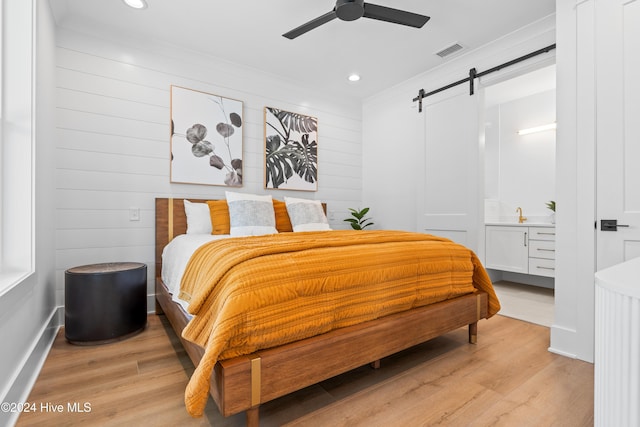 bedroom featuring ceiling fan, a barn door, and light hardwood / wood-style flooring