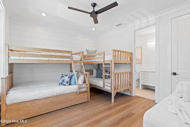 bedroom with ceiling fan, wooden walls, and light wood-type flooring