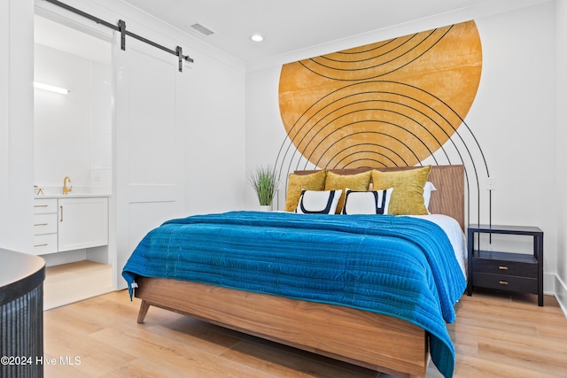 bedroom featuring a barn door, ornamental molding, and light wood-type flooring