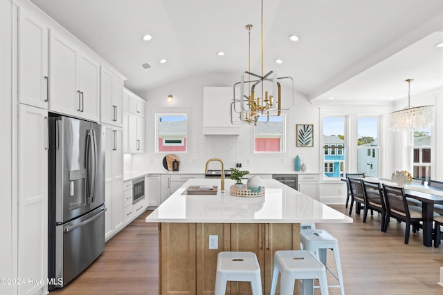 kitchen with lofted ceiling, backsplash, a kitchen island with sink, white cabinets, and appliances with stainless steel finishes