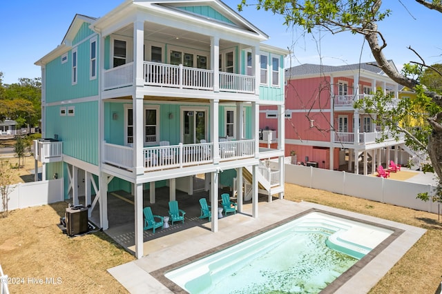 rear view of property featuring a fenced in pool, a patio area, a balcony, and cooling unit