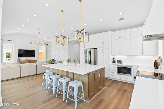 kitchen with white cabinetry, stainless steel appliances, an island with sink, lofted ceiling, and decorative light fixtures