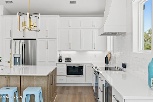 kitchen with white cabinets, custom exhaust hood, and appliances with stainless steel finishes