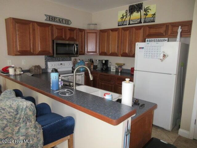 kitchen with a breakfast bar area, kitchen peninsula, light tile patterned flooring, and white appliances