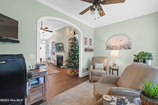 living area featuring crown molding, wood finished floors, baseboards, ceiling fan, and a fireplace with flush hearth