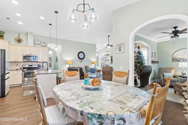 dining room with ornamental molding, sink, ceiling fan with notable chandelier, and light wood-type flooring