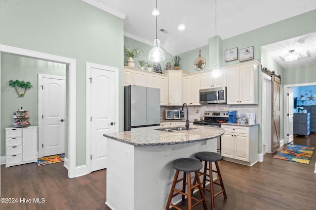 kitchen featuring sink, appliances with stainless steel finishes, an island with sink, decorative light fixtures, and a barn door