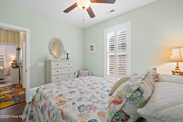 bedroom with multiple windows, a ceiling fan, wood finished floors, and visible vents