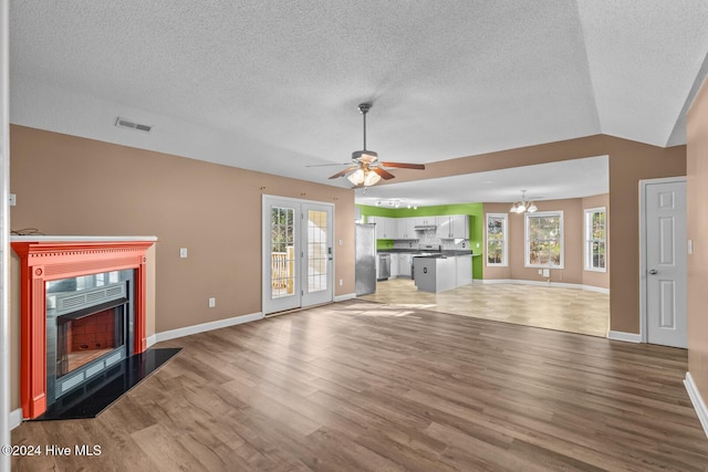 unfurnished living room featuring a textured ceiling, ceiling fan with notable chandelier, lofted ceiling, and hardwood / wood-style flooring