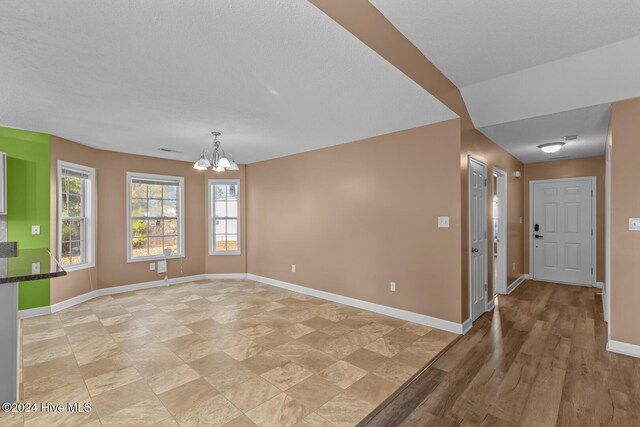 empty room with light hardwood / wood-style floors, a textured ceiling, and a notable chandelier