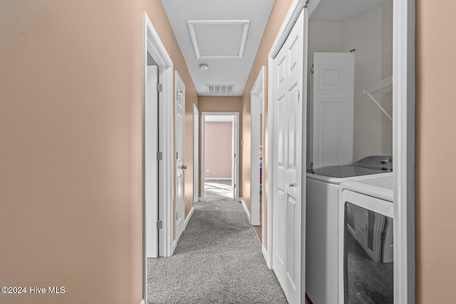 hallway with light carpet, a textured ceiling, and washer and clothes dryer