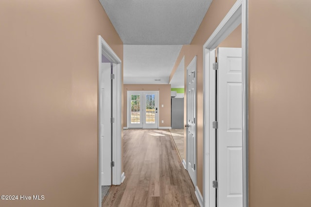 corridor with french doors, a textured ceiling, and light hardwood / wood-style flooring