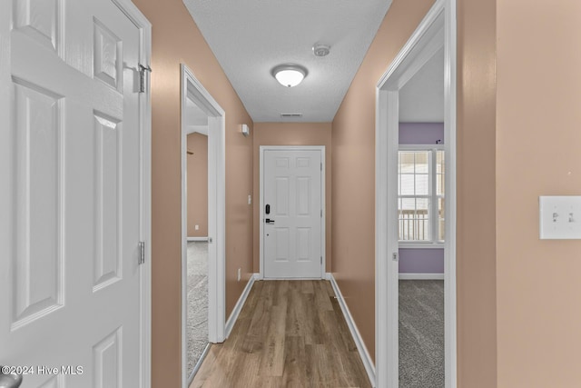 hallway with a textured ceiling and light hardwood / wood-style floors