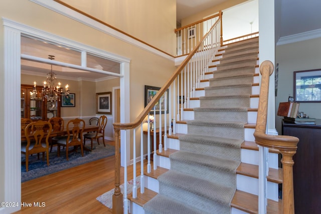 staircase with hardwood / wood-style flooring, crown molding, and a notable chandelier