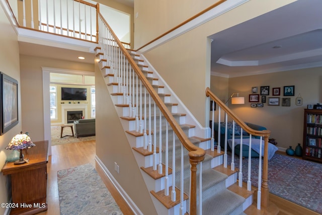 stairway with a raised ceiling, ornamental molding, and hardwood / wood-style flooring