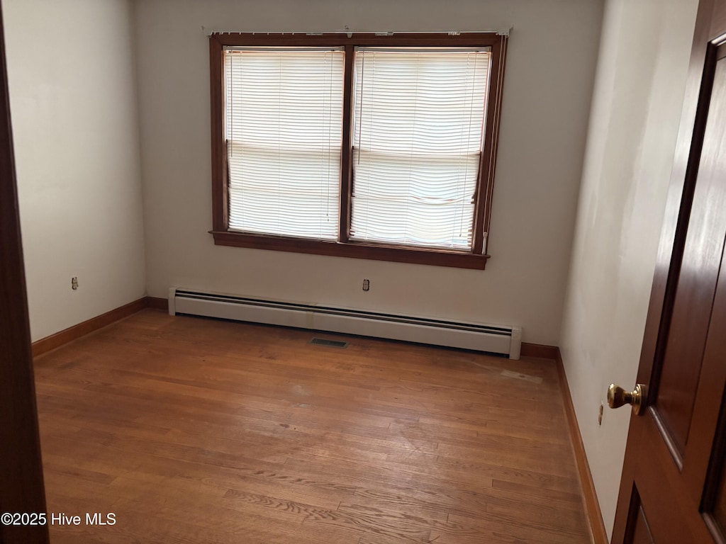 unfurnished room with baseboard heating and wood-type flooring