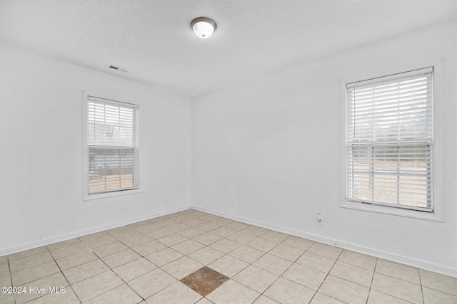 spare room featuring light tile patterned floors, a healthy amount of sunlight, and a textured ceiling