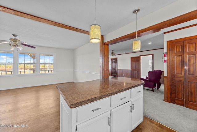 kitchen featuring a kitchen island, beamed ceiling, carpet floors, pendant lighting, and white cabinets