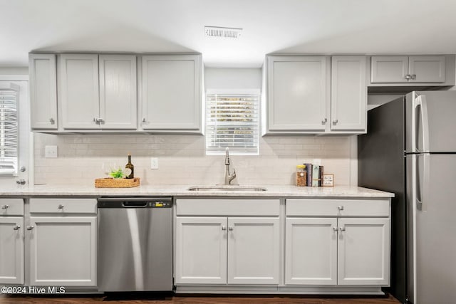 kitchen featuring light stone countertops, stainless steel appliances, a sink, visible vents, and decorative backsplash