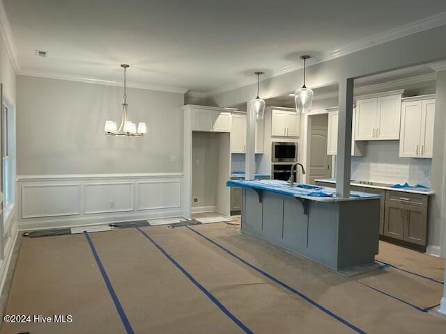 kitchen with white cabinets, hanging light fixtures, ornamental molding, an island with sink, and appliances with stainless steel finishes