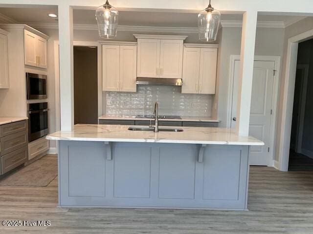 kitchen featuring decorative light fixtures, oven, white cabinets, and a center island with sink