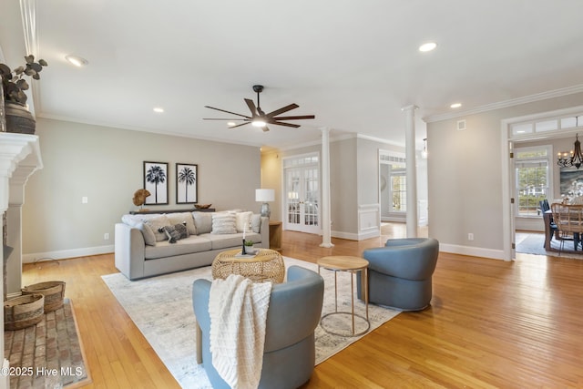 living room with decorative columns, light wood-type flooring, ceiling fan with notable chandelier, and ornamental molding