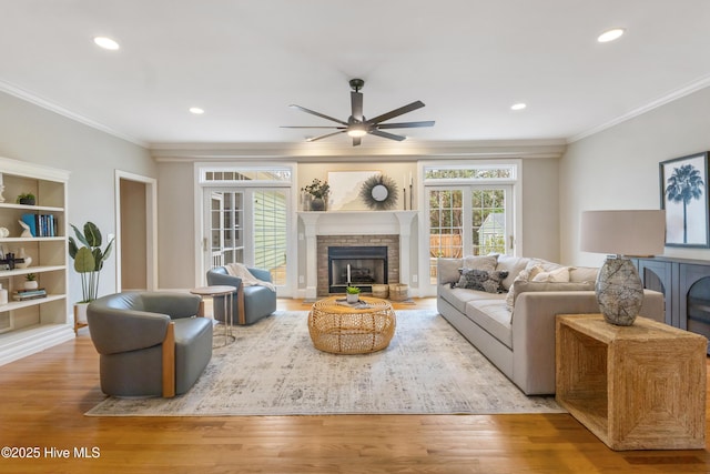 living room featuring ceiling fan, a brick fireplace, light hardwood / wood-style flooring, and crown molding