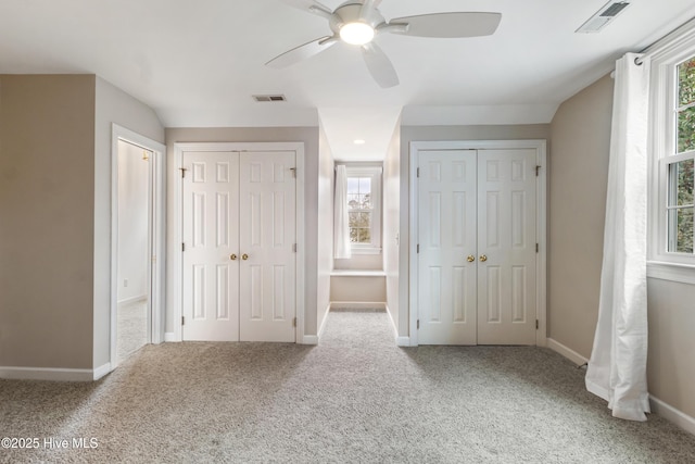 unfurnished bedroom featuring ceiling fan, carpet flooring, and two closets