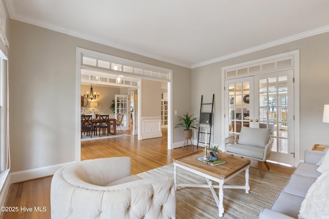 living room featuring wood-type flooring, ornamental molding, an inviting chandelier, and french doors