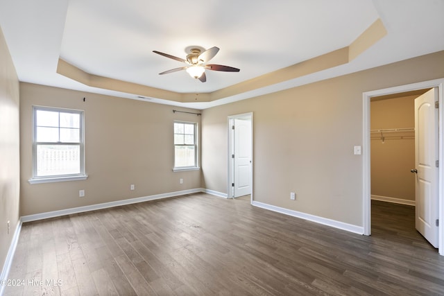 empty room with ceiling fan, dark hardwood / wood-style flooring, a wealth of natural light, and a tray ceiling