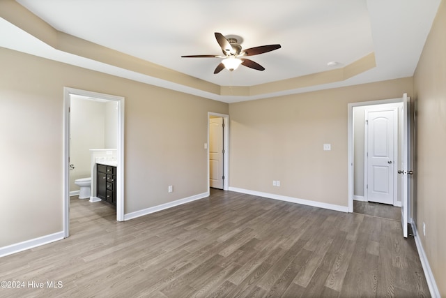 unfurnished bedroom featuring a tray ceiling, connected bathroom, ceiling fan, and hardwood / wood-style flooring