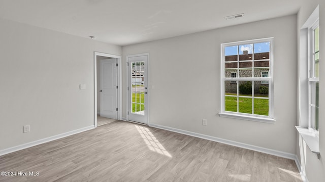 spare room with baseboards, wood finished floors, visible vents, and a healthy amount of sunlight