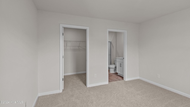 unfurnished bedroom with baseboards, ensuite bath, a spacious closet, carpet floors, and a closet