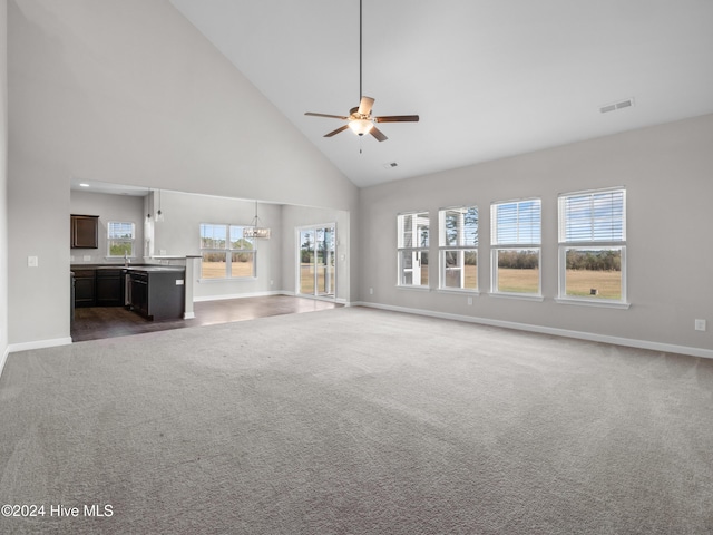 unfurnished living room featuring plenty of natural light, carpet floors, ceiling fan with notable chandelier, and high vaulted ceiling