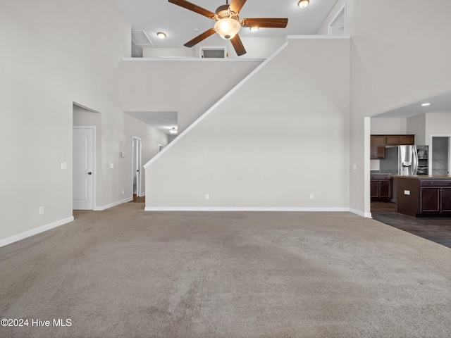 unfurnished living room featuring dark colored carpet, a high ceiling, and ceiling fan