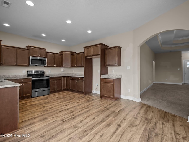 kitchen with crown molding, light wood-type flooring, stainless steel appliances, and a tray ceiling