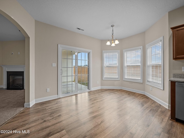 unfurnished dining area featuring a chandelier, a healthy amount of sunlight, a textured ceiling, and light hardwood / wood-style flooring