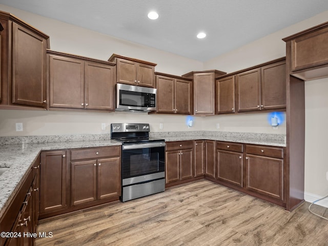 kitchen with dark brown cabinetry, light stone countertops, stainless steel appliances, and light wood-type flooring