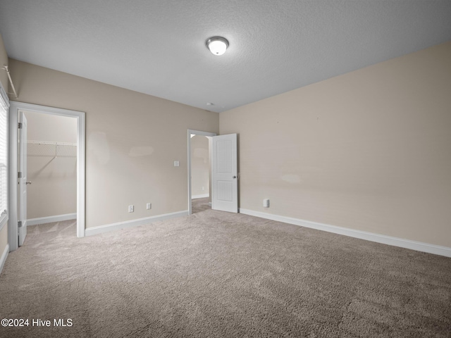 unfurnished bedroom with carpet flooring, a spacious closet, a textured ceiling, and a closet