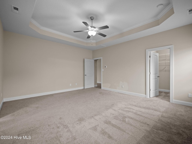 unfurnished bedroom with a raised ceiling, a spacious closet, ceiling fan, and ornamental molding