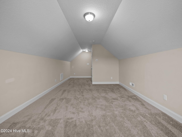 additional living space with a textured ceiling, light colored carpet, and lofted ceiling