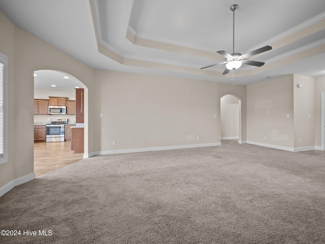 carpeted empty room featuring a raised ceiling, crown molding, and ceiling fan