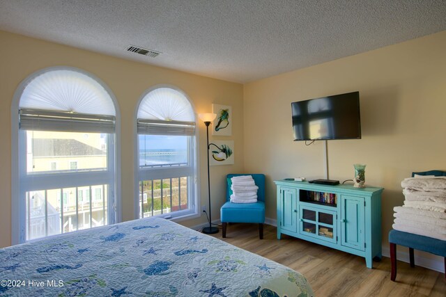 bedroom featuring ensuite bath, light hardwood / wood-style floors, a textured ceiling, and fridge