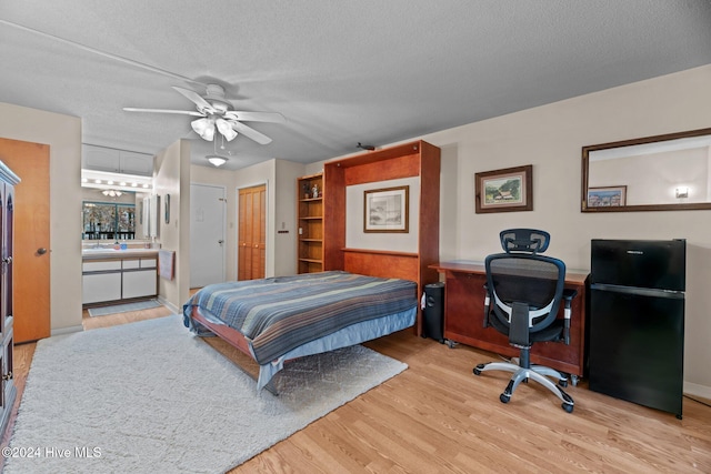 bedroom featuring ceiling fan, black fridge, ensuite bathroom, light hardwood / wood-style floors, and a textured ceiling