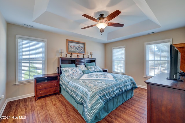 bedroom featuring light hardwood / wood-style flooring, a raised ceiling, and ceiling fan