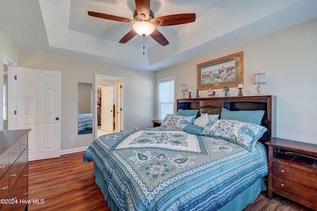 bedroom with ensuite bath, dark hardwood / wood-style floors, a raised ceiling, and ceiling fan