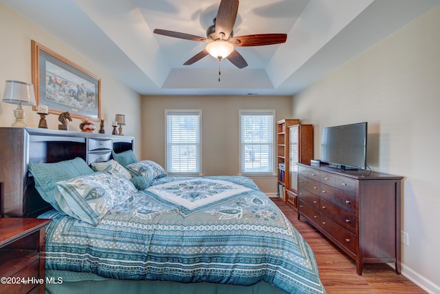 bedroom with ceiling fan, light hardwood / wood-style flooring, and a tray ceiling