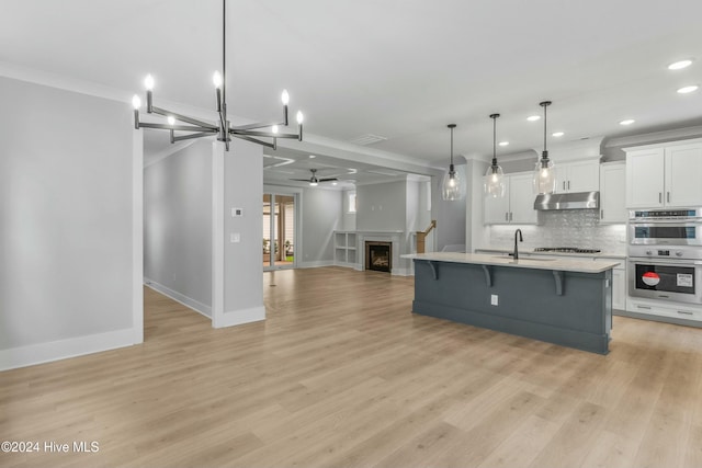 kitchen with appliances with stainless steel finishes, pendant lighting, white cabinetry, a kitchen breakfast bar, and a center island with sink