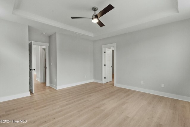 empty room with ceiling fan, a tray ceiling, and light hardwood / wood-style floors